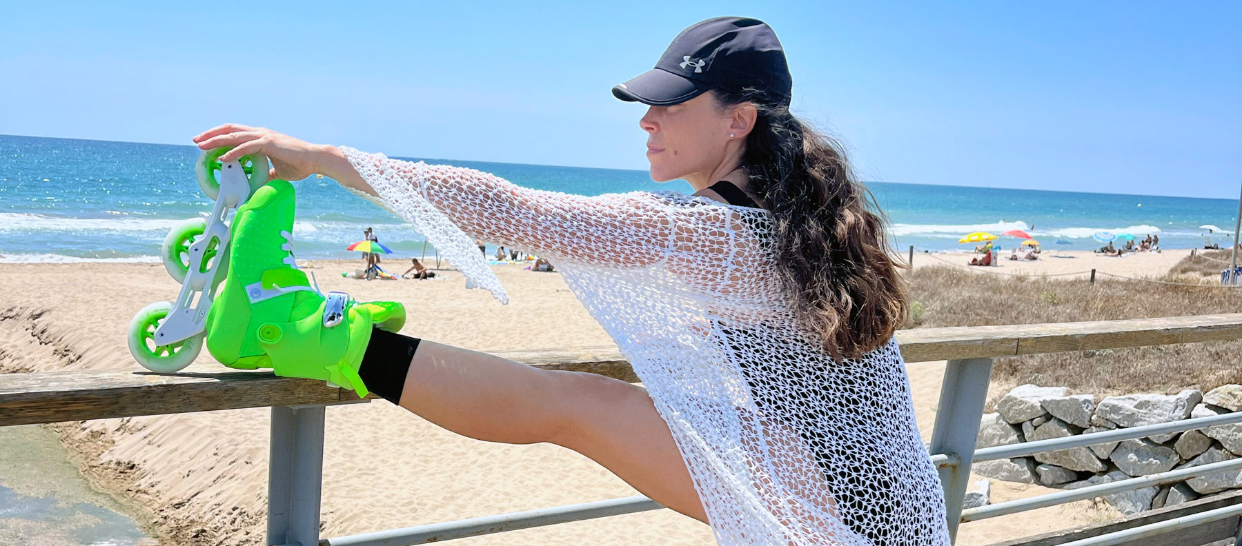 Powerslide fitness skater Judit Abarca is stretching her leg on a handrail at the beach.